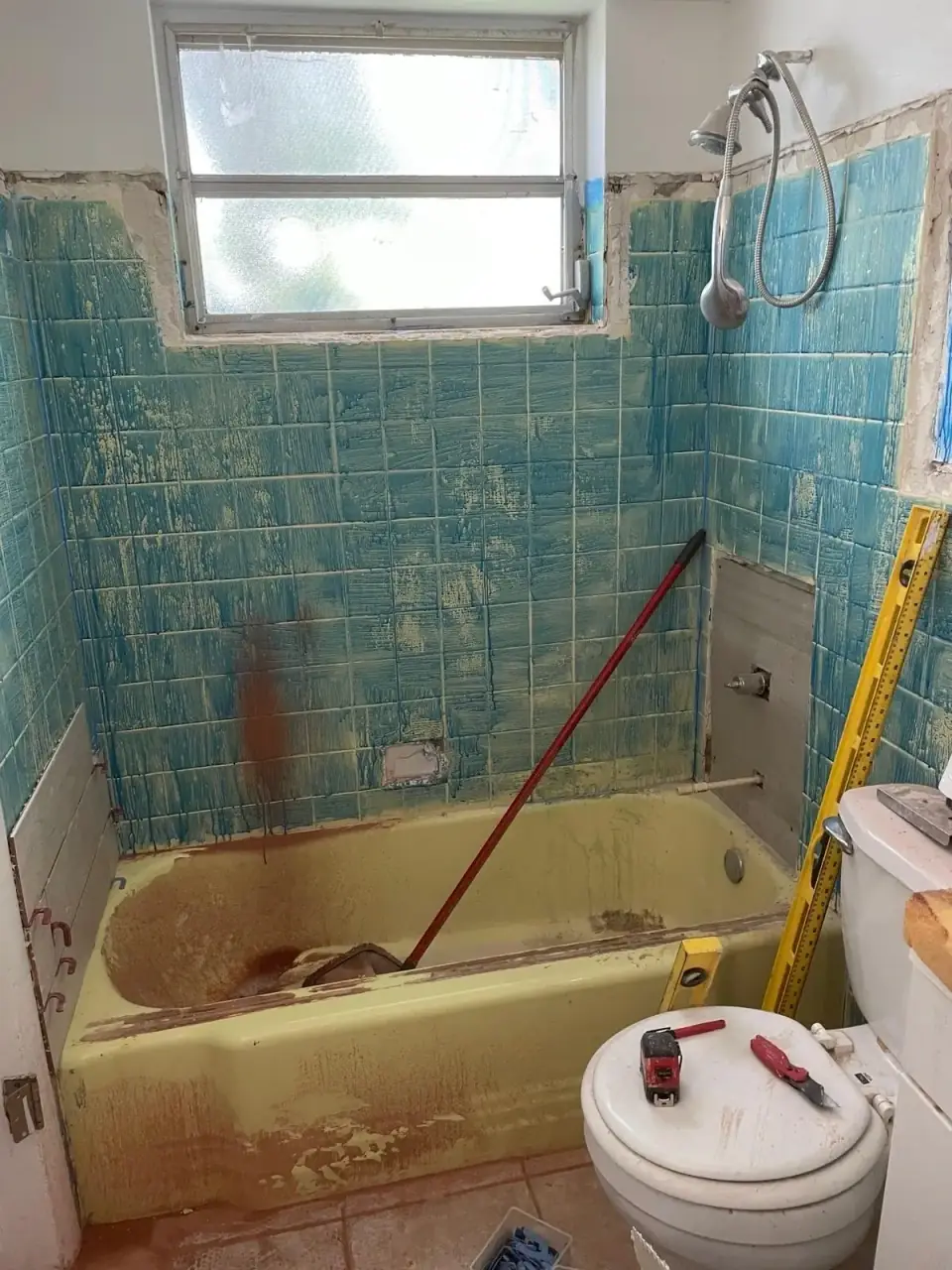 Before: Outdated bathroom before renovation with old turquoise tile and yellow tub in Miami home.