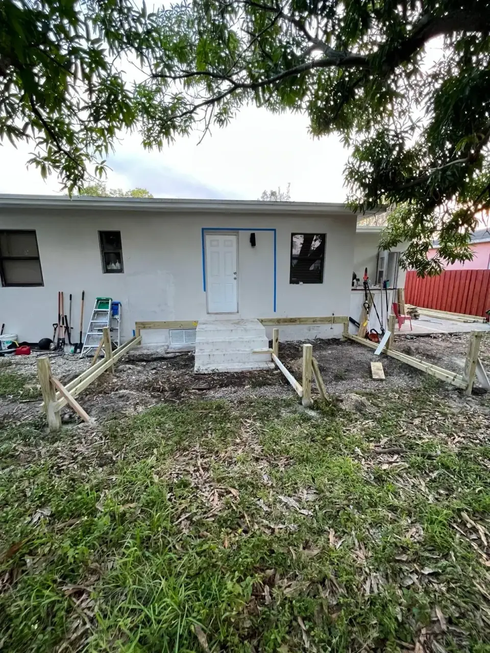 Before: Backyard area before deck construction with white concrete steps and wood framing - Miami